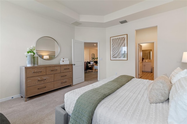 bedroom with light colored carpet, a raised ceiling, and ensuite bathroom