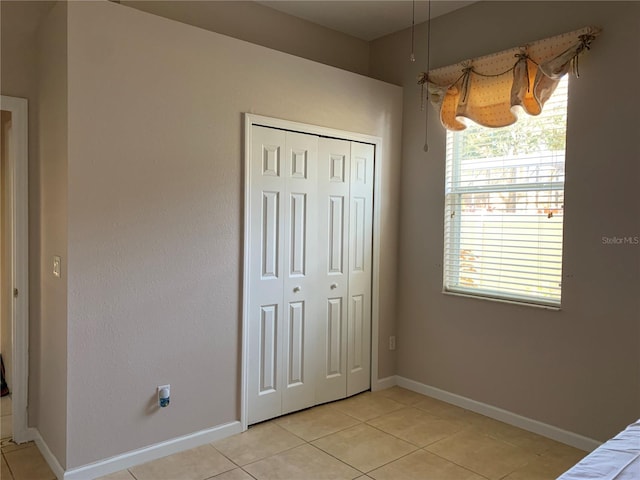 unfurnished bedroom with multiple windows, light tile patterned floors, and a closet