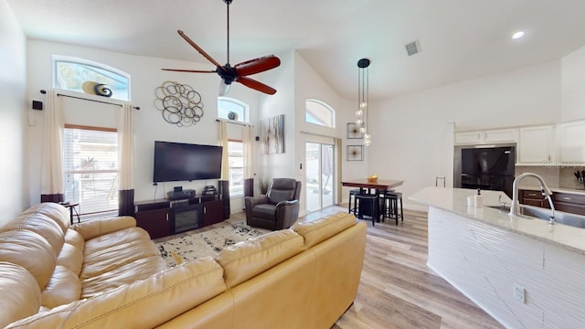 living room featuring ceiling fan, light hardwood / wood-style floors, sink, and high vaulted ceiling