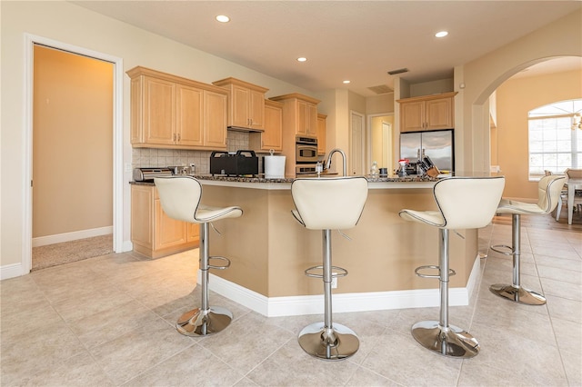 kitchen featuring light brown cabinetry, tasteful backsplash, a breakfast bar, stainless steel refrigerator, and an island with sink