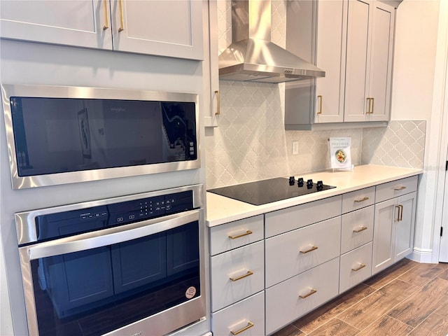 kitchen featuring decorative backsplash, light wood-type flooring, stainless steel appliances, and wall chimney range hood