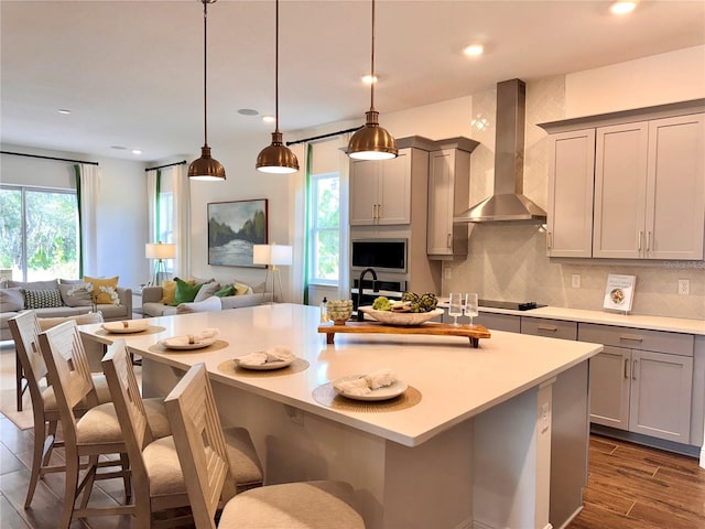 kitchen featuring gray cabinetry, dark hardwood / wood-style floors, wall chimney range hood, and a breakfast bar area