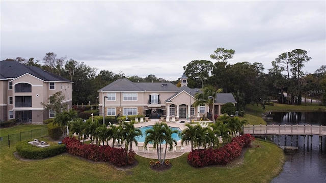 rear view of house featuring a lawn, a water view, a fenced in pool, and a patio