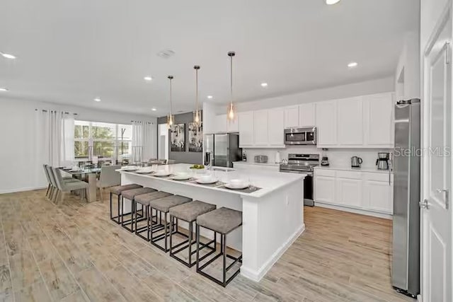 kitchen with white cabinets, appliances with stainless steel finishes, light wood-type flooring, and a large island with sink