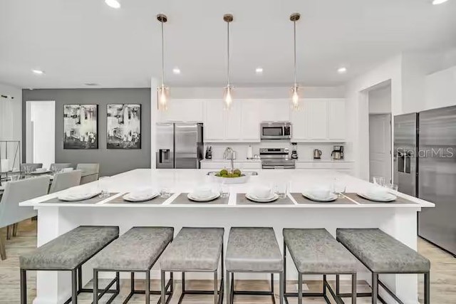 kitchen with a breakfast bar, stainless steel appliances, white cabinetry, hanging light fixtures, and a large island