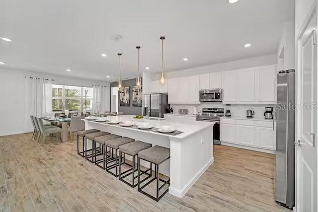 kitchen with light wood-type flooring, stainless steel appliances, white cabinetry, and a spacious island