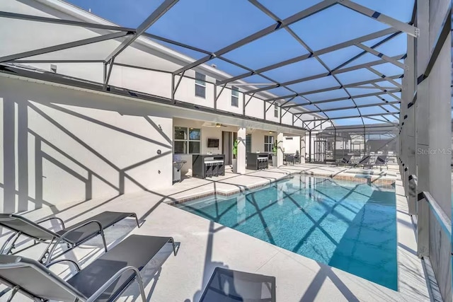 view of pool with glass enclosure, ceiling fan, a patio, and an outdoor kitchen