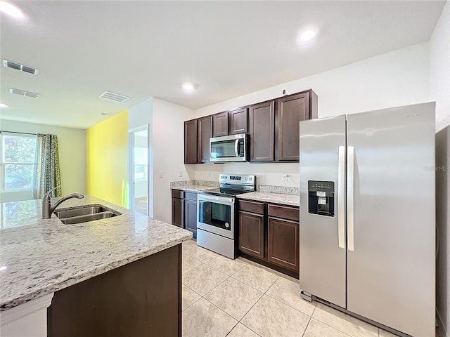 kitchen featuring sink, light tile patterned floors, light stone counters, dark brown cabinetry, and stainless steel appliances