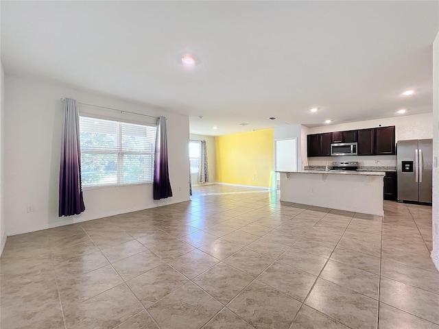 kitchen with dark brown cabinetry, stainless steel appliances, a kitchen breakfast bar, a kitchen island with sink, and light tile patterned flooring