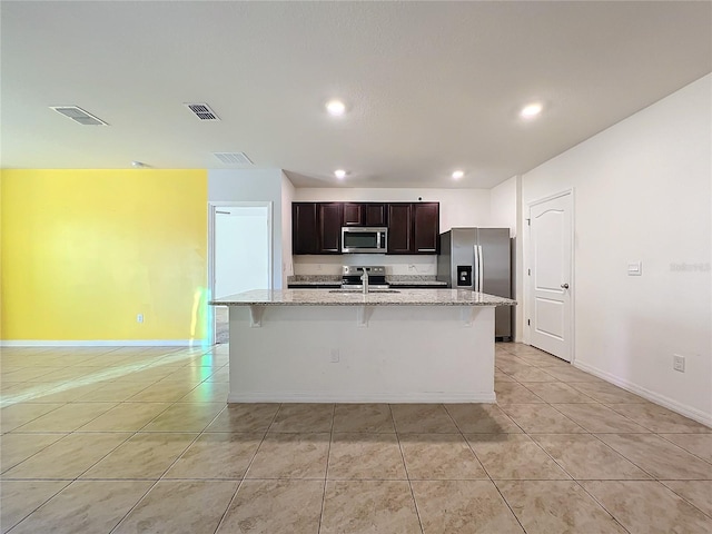 kitchen featuring a kitchen island with sink, sink, appliances with stainless steel finishes, light stone counters, and dark brown cabinetry