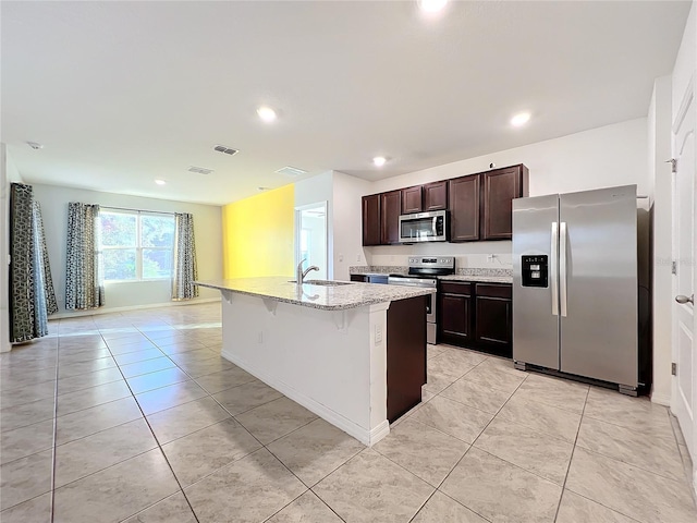 kitchen with sink, a breakfast bar area, an island with sink, light stone counters, and stainless steel appliances