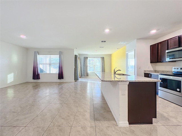 kitchen featuring stainless steel appliances, plenty of natural light, a kitchen island with sink, and light stone counters