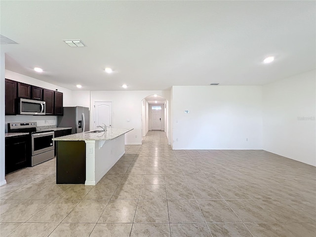 kitchen featuring light stone countertops, sink, stainless steel appliances, a kitchen island with sink, and a breakfast bar