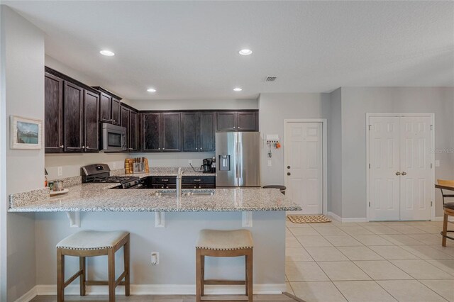 kitchen with appliances with stainless steel finishes, a breakfast bar, sink, light tile patterned floors, and light stone counters