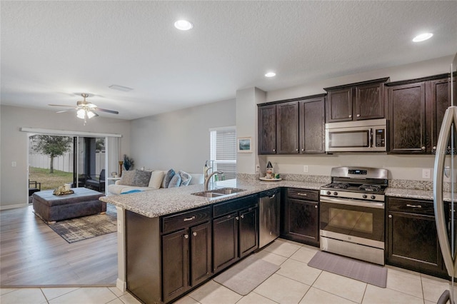 kitchen with dark brown cabinetry, sink, light tile patterned floors, kitchen peninsula, and stainless steel appliances