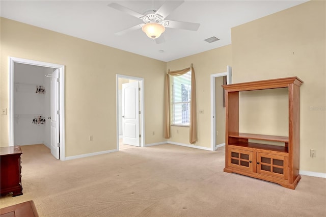 unfurnished bedroom with a walk in closet, light colored carpet, a closet, and ceiling fan