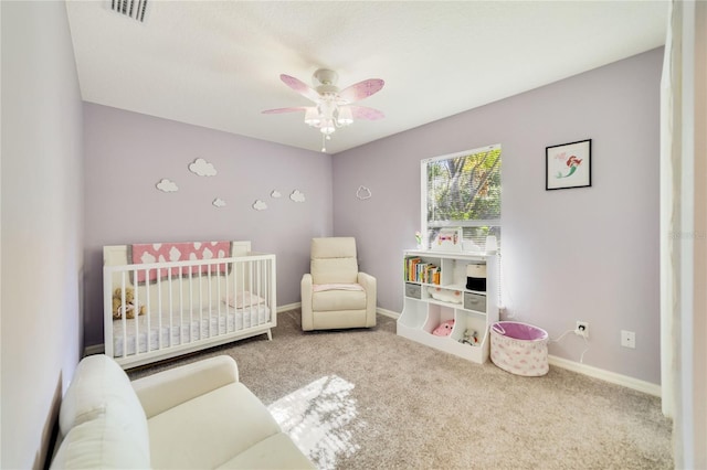 carpeted bedroom with ceiling fan and a nursery area