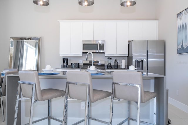 kitchen with white cabinetry, stainless steel appliances, light tile patterned floors, and a breakfast bar area