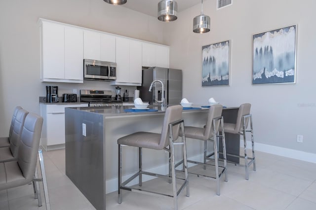 kitchen featuring pendant lighting, a kitchen island with sink, white cabinets, appliances with stainless steel finishes, and a breakfast bar area