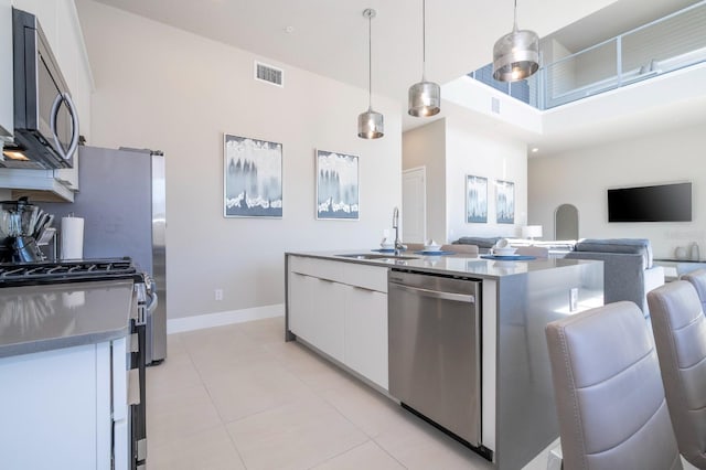 kitchen featuring stainless steel appliances, sink, light tile patterned floors, decorative light fixtures, and white cabinetry