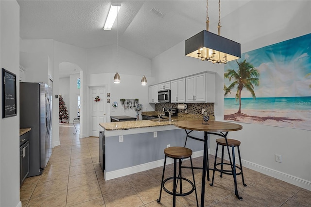 kitchen featuring white cabinets, a kitchen breakfast bar, a textured ceiling, appliances with stainless steel finishes, and kitchen peninsula