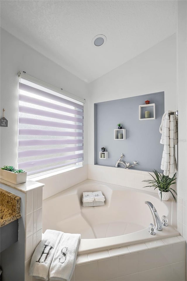 bathroom with a textured ceiling, vaulted ceiling, and tiled tub