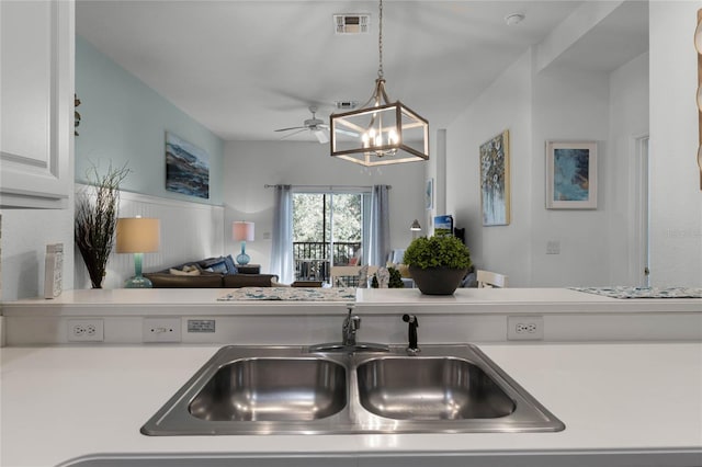 kitchen featuring sink, hanging light fixtures, stovetop, white cabinets, and ceiling fan with notable chandelier