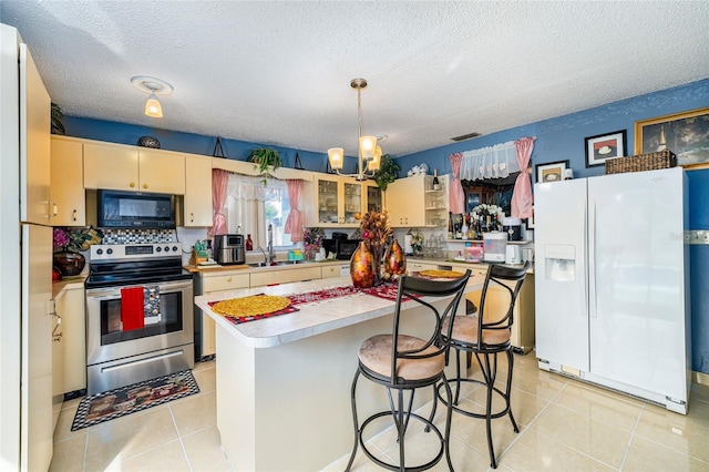 kitchen featuring light tile patterned floors, white fridge with ice dispenser, a textured ceiling, stainless steel electric range oven, and decorative light fixtures