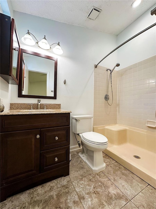 bathroom featuring vanity, a tile shower, a textured ceiling, and toilet