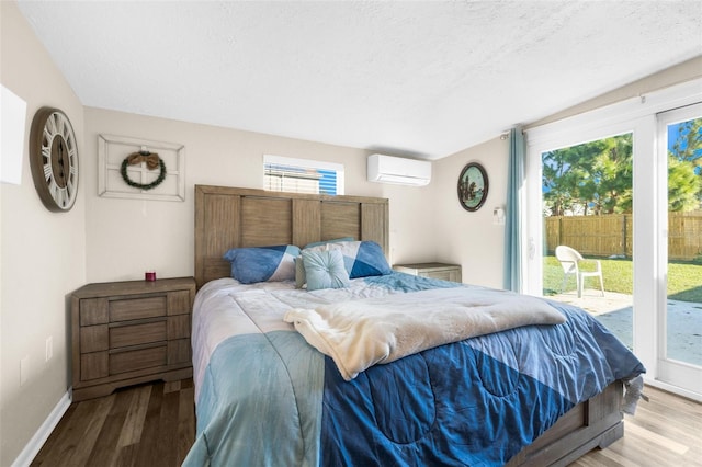 bedroom featuring access to outside, a wall unit AC, wood-type flooring, and a textured ceiling