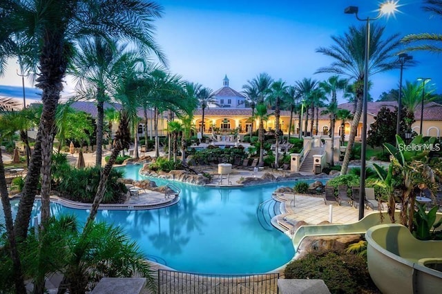 pool at dusk featuring a patio area, stairway, and a community pool