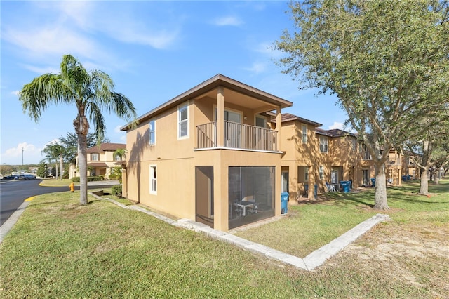 rear view of house with a yard, a balcony, and stucco siding