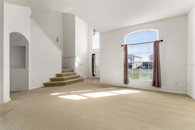 unfurnished living room with light carpet, a high ceiling, and a textured ceiling