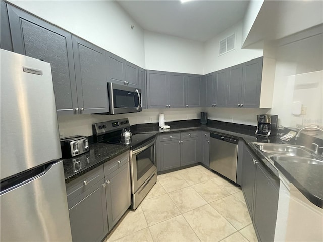 kitchen featuring sink, gray cabinets, dark stone countertops, light tile patterned floors, and stainless steel appliances