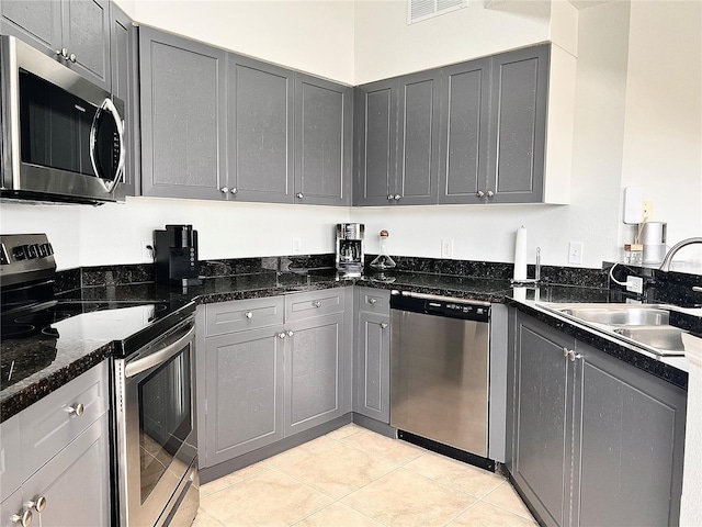 kitchen featuring gray cabinetry, dark stone countertops, sink, and appliances with stainless steel finishes