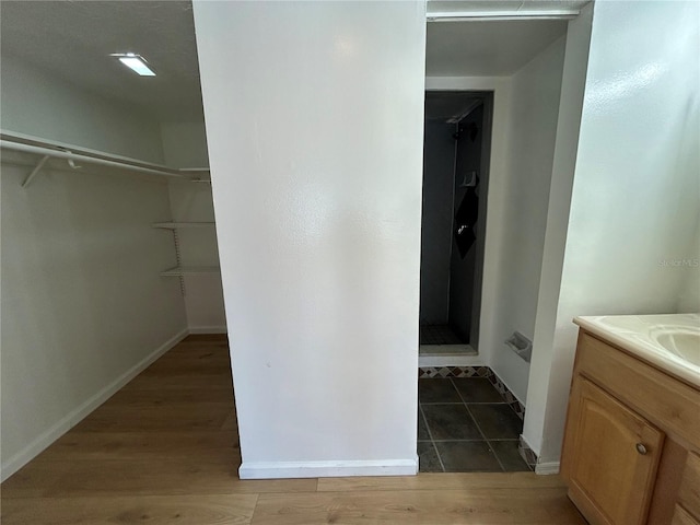 bathroom with a walk in closet, a stall shower, wood finished floors, baseboards, and vanity