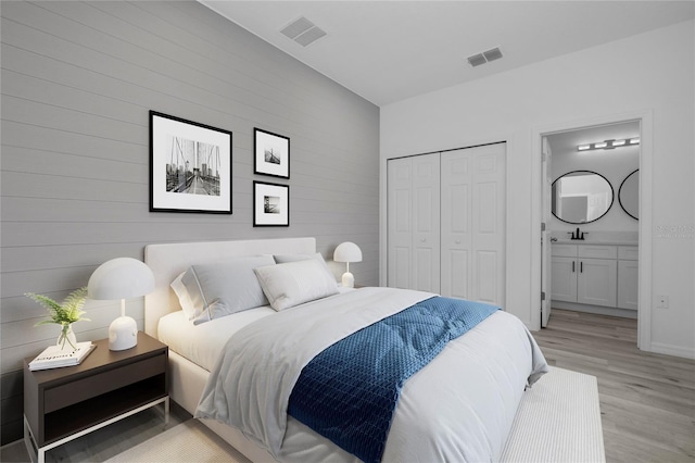 bedroom with light wood-type flooring, a closet, connected bathroom, and sink