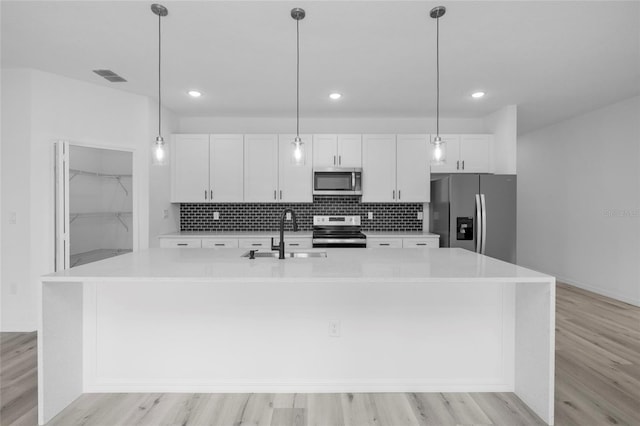 kitchen featuring white cabinetry, an island with sink, appliances with stainless steel finishes, decorative light fixtures, and sink