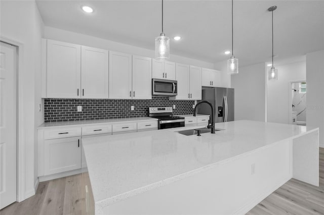 kitchen with stainless steel appliances, white cabinets, a center island with sink, and sink