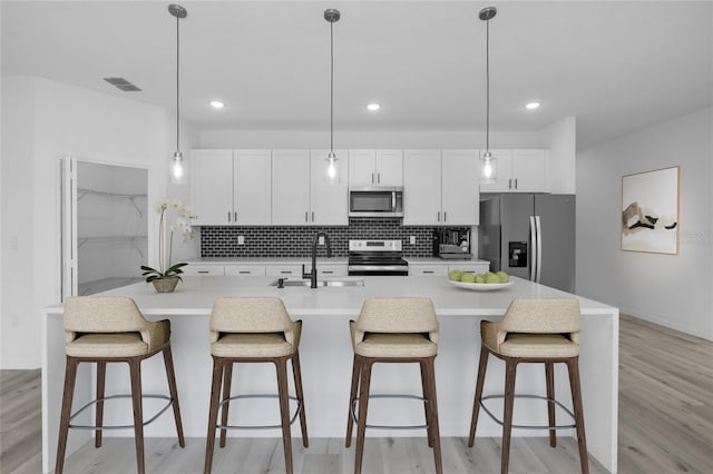 kitchen with white cabinetry, a center island with sink, stainless steel appliances, decorative light fixtures, and sink