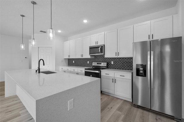 kitchen with white cabinets, appliances with stainless steel finishes, decorative light fixtures, an island with sink, and sink