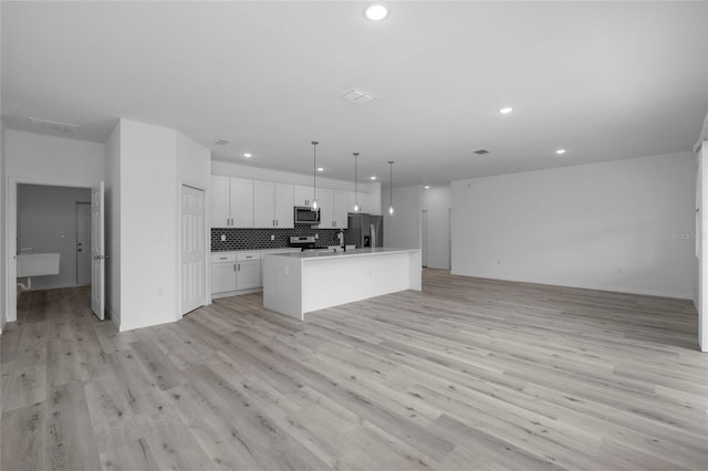 kitchen featuring pendant lighting, appliances with stainless steel finishes, white cabinetry, backsplash, and a kitchen island with sink