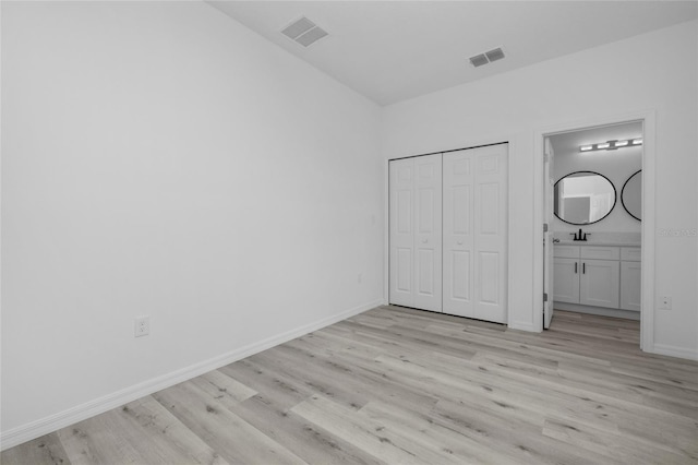 unfurnished bedroom featuring a closet, sink, connected bathroom, and light hardwood / wood-style floors