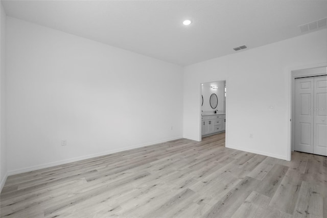 unfurnished bedroom featuring ensuite bathroom, a closet, and light hardwood / wood-style flooring