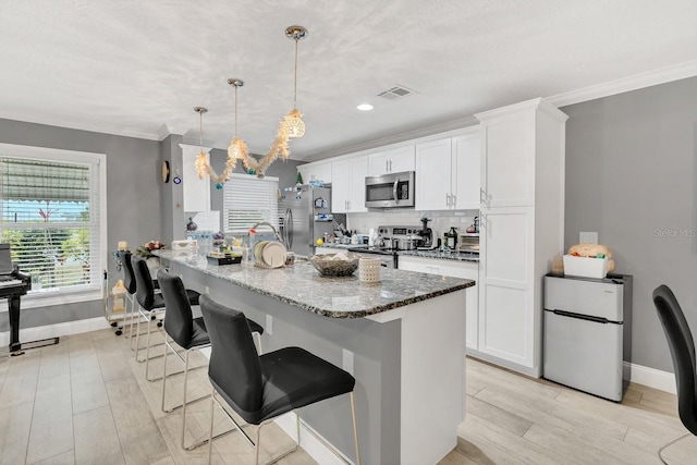 kitchen featuring a breakfast bar area, appliances with stainless steel finishes, light stone countertops, white cabinetry, and decorative light fixtures