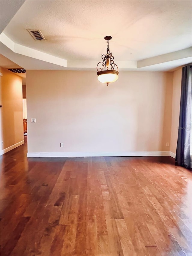 unfurnished room with wood-type flooring, a textured ceiling, and a tray ceiling