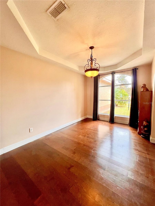 spare room with a raised ceiling, wood-type flooring, and a textured ceiling