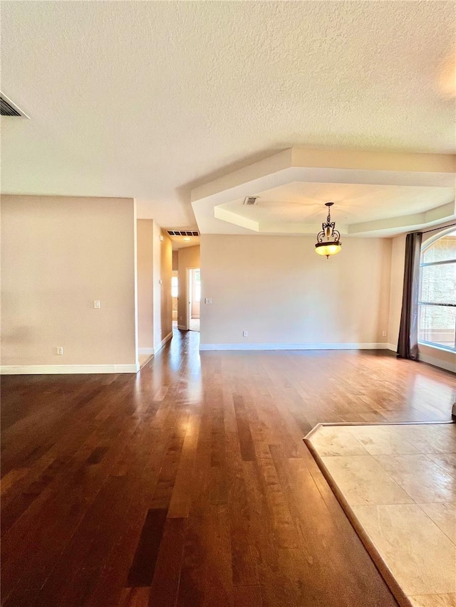 spare room featuring a tray ceiling, wood-type flooring, and a textured ceiling