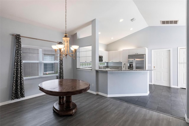 kitchen featuring stainless steel appliances, vaulted ceiling, dark wood-type flooring, decorative light fixtures, and white cabinetry