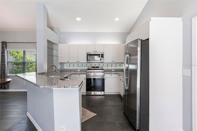 kitchen with kitchen peninsula, appliances with stainless steel finishes, white cabinets, and sink